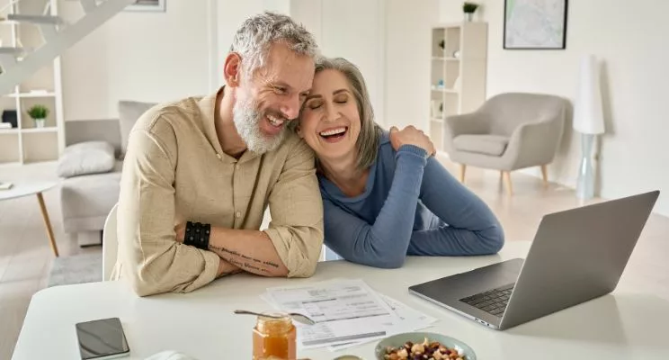 Middle-aged married couple sitting next to each other behind kitchen counter laughing